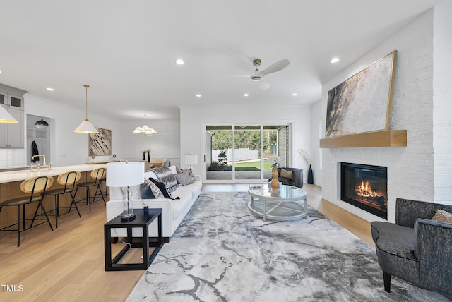 living room with ceiling fan, a large fireplace, light wood-type flooring, and sink