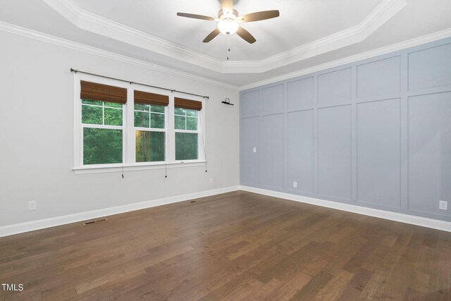 empty room featuring dark wood-type flooring, a raised ceiling, and ornamental molding