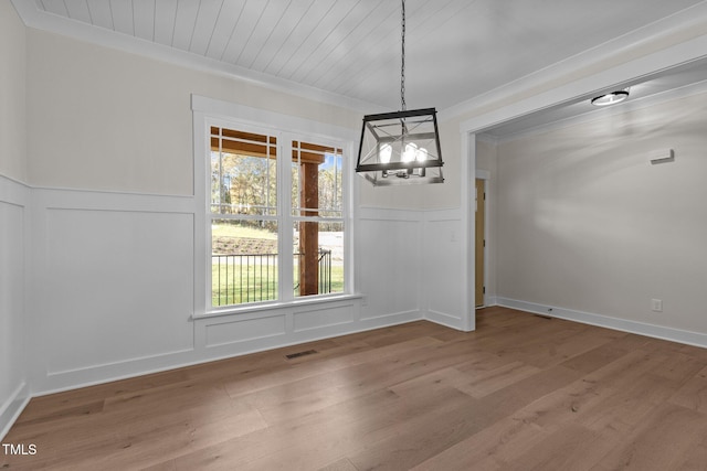 unfurnished dining area featuring wood-type flooring, crown molding, and a chandelier