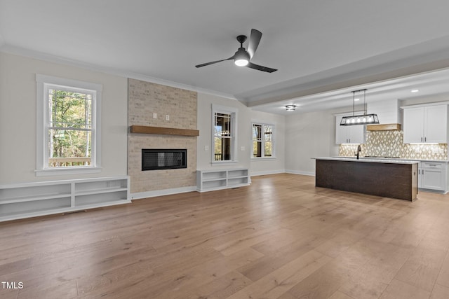 unfurnished living room featuring ceiling fan, crown molding, a fireplace, and light hardwood / wood-style flooring