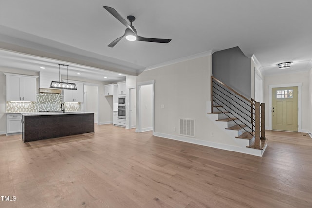 unfurnished living room featuring crown molding, ceiling fan, sink, and light hardwood / wood-style floors