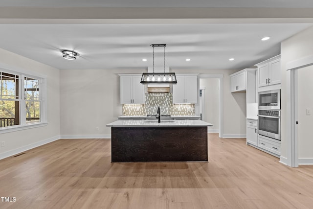 kitchen featuring an island with sink, sink, white cabinets, hanging light fixtures, and stainless steel oven