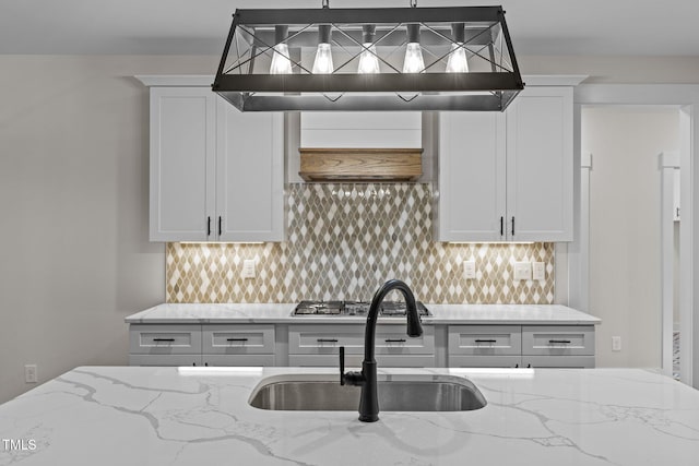 kitchen with tasteful backsplash, stainless steel gas cooktop, range hood, light stone counters, and sink