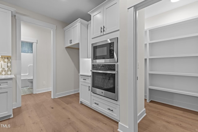 kitchen featuring backsplash, light hardwood / wood-style floors, stainless steel oven, built in microwave, and white cabinets