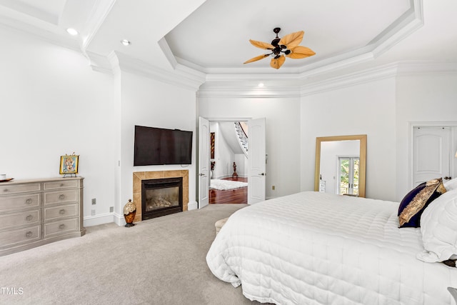 carpeted bedroom featuring crown molding, a fireplace, a raised ceiling, and ceiling fan