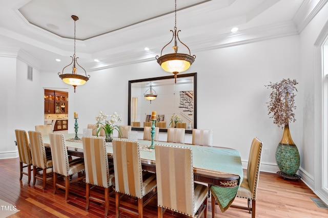 dining room featuring crown molding, light hardwood / wood-style flooring, and a raised ceiling