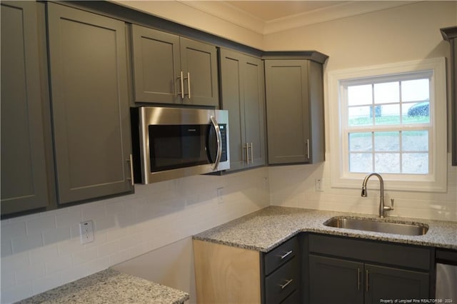 kitchen with ornamental molding, a sink, stainless steel microwave, light stone counters, and decorative backsplash