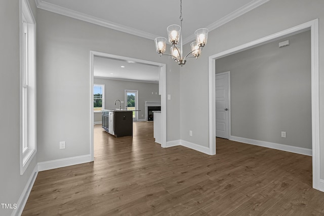 unfurnished dining area featuring sink, ornamental molding, dark wood-type flooring, and an inviting chandelier