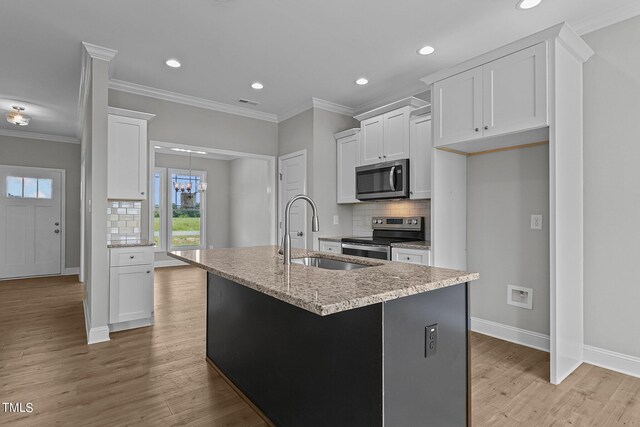 kitchen with decorative backsplash, a kitchen island with sink, light hardwood / wood-style floors, stainless steel appliances, and sink