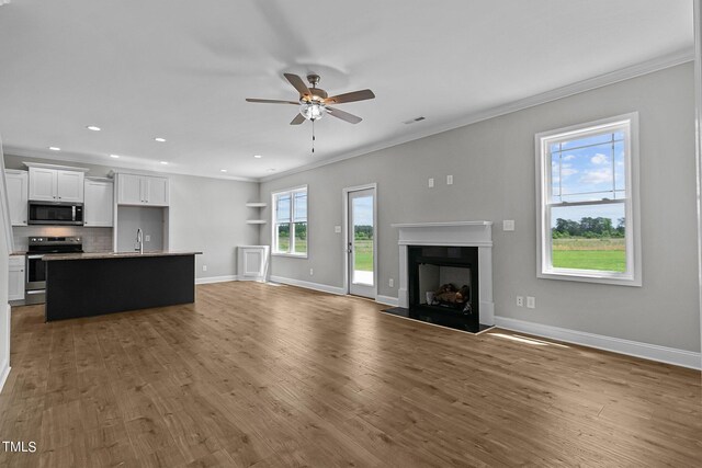 unfurnished living room with ceiling fan, sink, light wood-type flooring, and ornamental molding