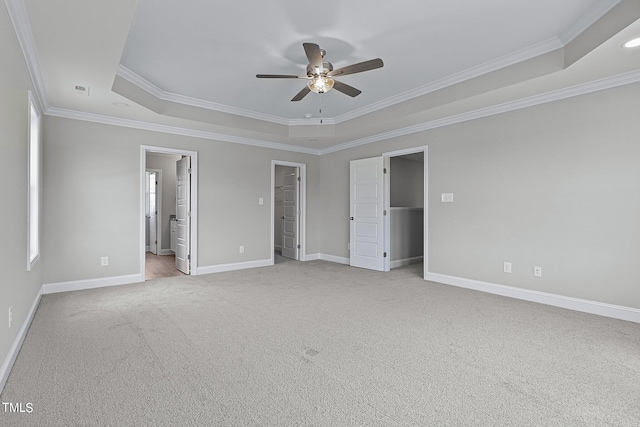 unfurnished bedroom featuring ceiling fan, a walk in closet, connected bathroom, carpet, and a tray ceiling