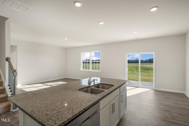 kitchen featuring a kitchen island with sink, dark stone countertops, hardwood / wood-style floors, sink, and white cabinetry