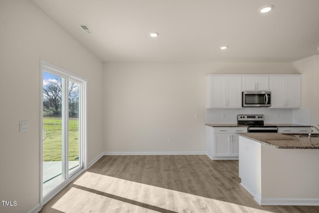 kitchen featuring white cabinets, tasteful backsplash, dark stone counters, light wood-type flooring, and stainless steel appliances