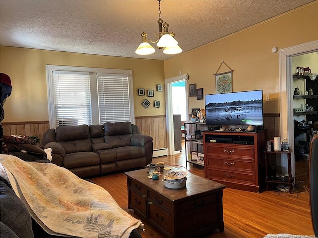 living room featuring an inviting chandelier, baseboard heating, a textured ceiling, and hardwood / wood-style flooring