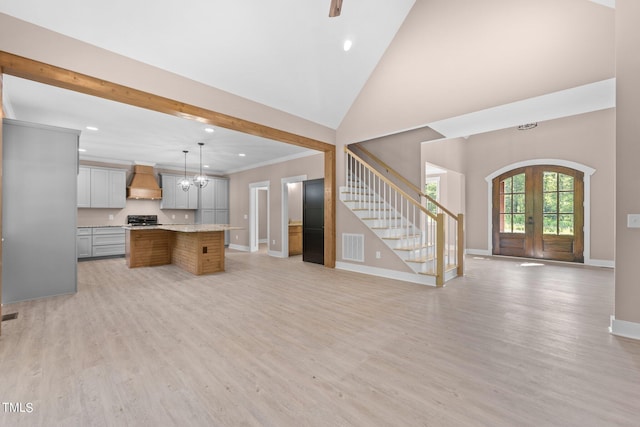 unfurnished living room featuring french doors, a chandelier, a high ceiling, and light wood-type flooring