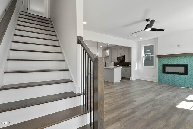 stairway featuring a tiled fireplace, ceiling fan, and hardwood / wood-style flooring