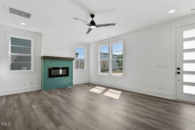 unfurnished living room with a tiled fireplace, ceiling fan, and dark wood-type flooring