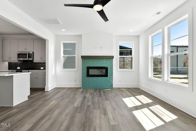 kitchen with a tile fireplace, backsplash, gray cabinets, light wood-type flooring, and ceiling fan