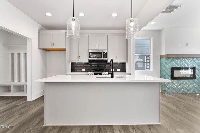 kitchen featuring pendant lighting, an island with sink, light hardwood / wood-style floors, and sink