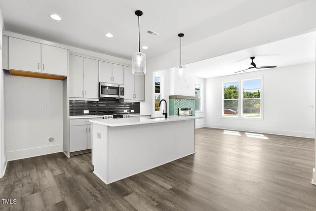 kitchen with appliances with stainless steel finishes, white cabinets, dark hardwood / wood-style flooring, ceiling fan, and a kitchen island with sink