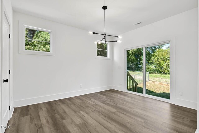 unfurnished room with an inviting chandelier, hardwood / wood-style flooring, and plenty of natural light