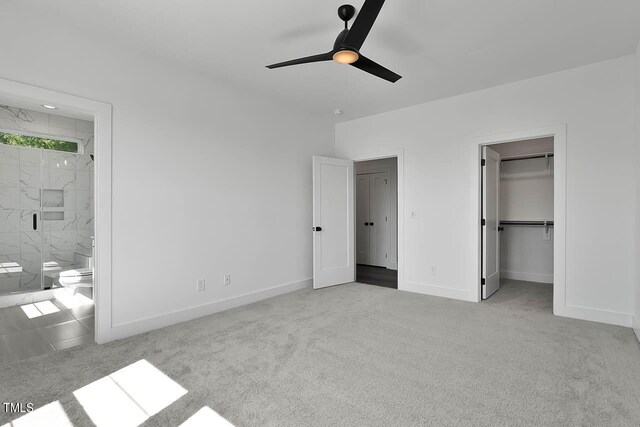 unfurnished bedroom featuring ceiling fan, connected bathroom, light carpet, and a walk in closet