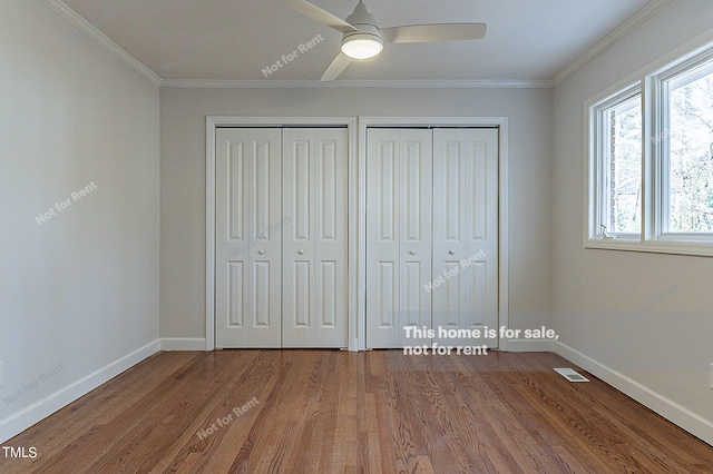 unfurnished bedroom with crown molding, dark hardwood / wood-style floors, ceiling fan, and two closets