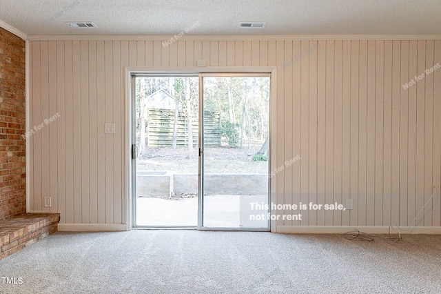 doorway with a textured ceiling, brick wall, crown molding, and light colored carpet