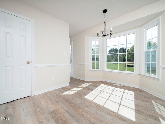 spare room with a notable chandelier, a wealth of natural light, and light hardwood / wood-style floors