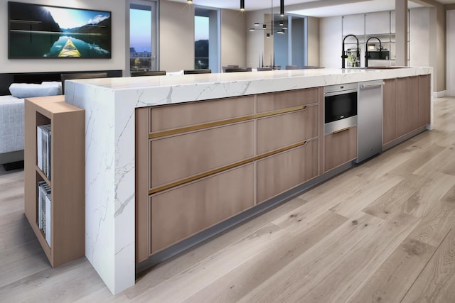 kitchen featuring stainless steel oven, light hardwood / wood-style floors, a kitchen island with sink, and light stone counters