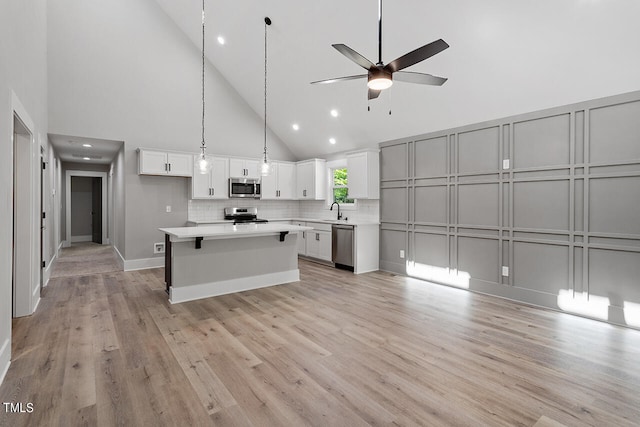 kitchen featuring pendant lighting, white cabinets, high vaulted ceiling, light hardwood / wood-style flooring, and appliances with stainless steel finishes