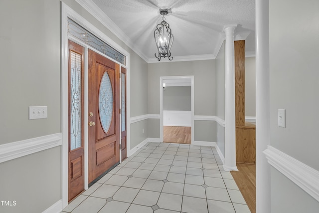 entrance foyer featuring a chandelier, ornamental molding, a textured ceiling, and decorative columns