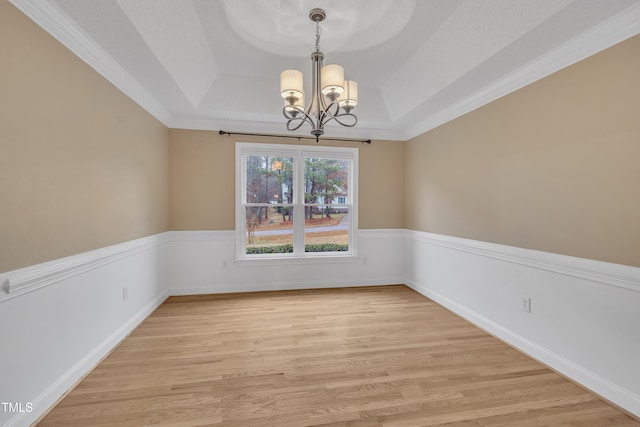 spare room with a chandelier, light wood-type flooring, a raised ceiling, and crown molding