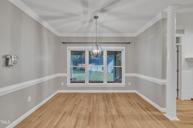 unfurnished dining area featuring ornate columns, crown molding, hardwood / wood-style flooring, and an inviting chandelier