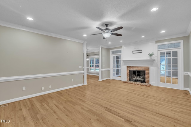 unfurnished living room with light wood-type flooring, a brick fireplace, ornamental molding, a textured ceiling, and ceiling fan