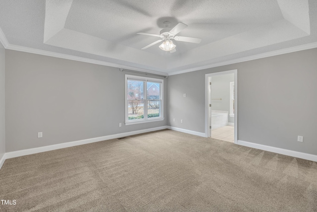 empty room featuring a raised ceiling, ceiling fan, ornamental molding, a textured ceiling, and light colored carpet