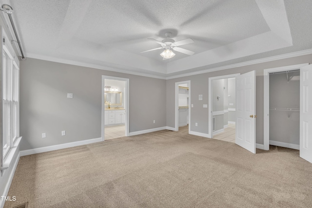 unfurnished bedroom featuring light carpet, ensuite bath, a tray ceiling, ceiling fan, and crown molding