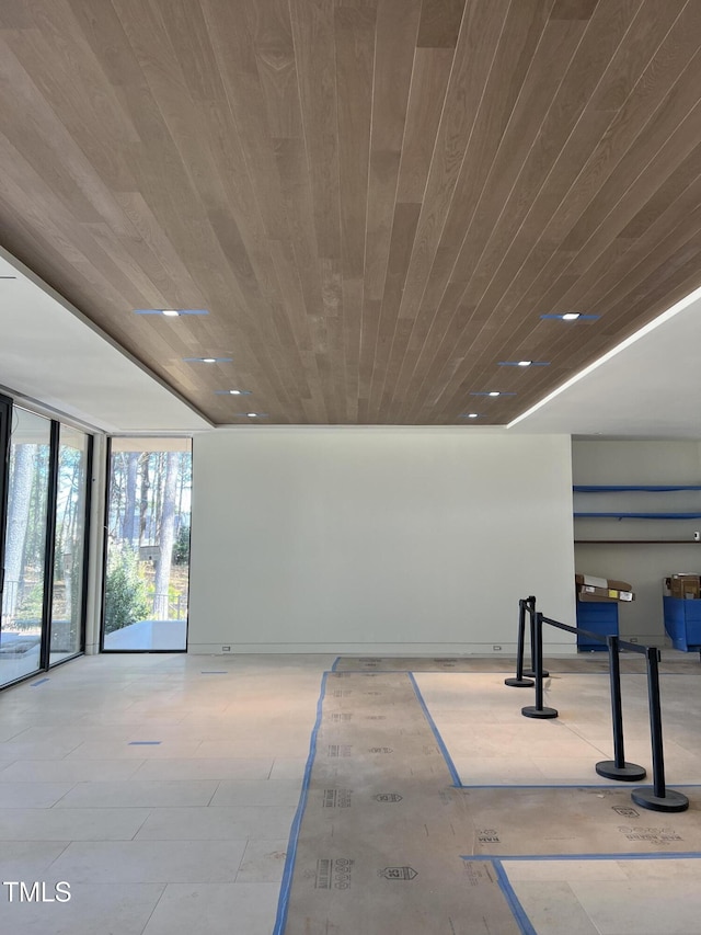 empty room featuring a wall of windows, wooden ceiling, and baseboards