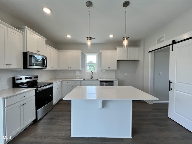 kitchen with appliances with stainless steel finishes, dark hardwood / wood-style floors, a barn door, and decorative backsplash