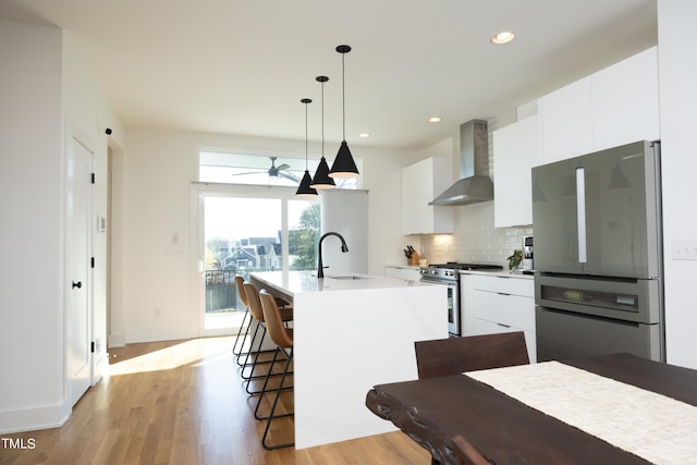 kitchen featuring appliances with stainless steel finishes, pendant lighting, sink, light hardwood / wood-style flooring, and wall chimney exhaust hood