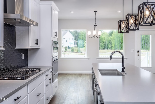 kitchen with wall chimney exhaust hood, sink, hanging light fixtures, stainless steel appliances, and wood-type flooring