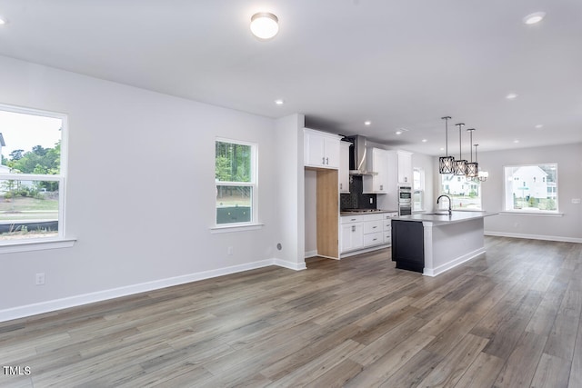 kitchen featuring wood-type flooring, a healthy amount of sunlight, wall chimney range hood, and a kitchen island with sink