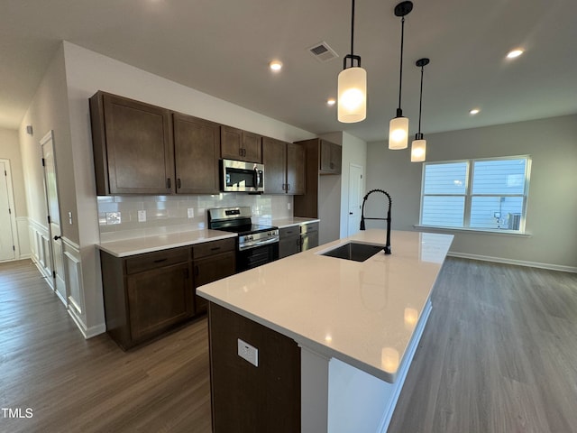 kitchen featuring appliances with stainless steel finishes, an island with sink, decorative light fixtures, and sink