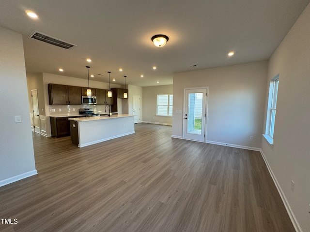 kitchen with dark brown cabinetry, dark hardwood / wood-style floors, an island with sink, decorative light fixtures, and appliances with stainless steel finishes