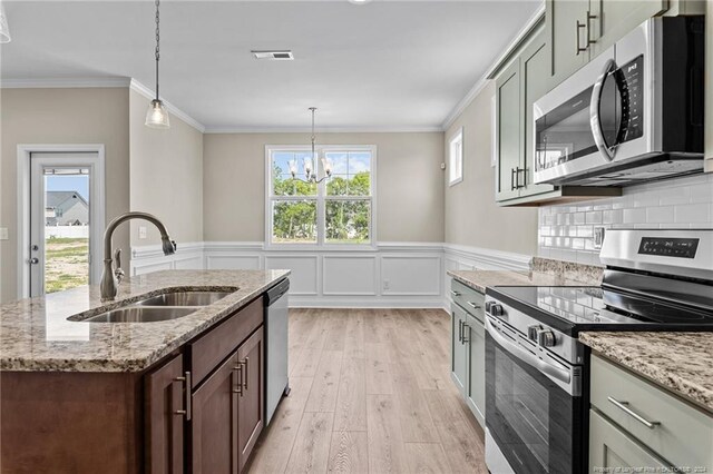 kitchen with stainless steel appliances, sink, light stone counters, hanging light fixtures, and light wood-type flooring