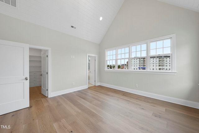 unfurnished bedroom with light hardwood / wood-style flooring, high vaulted ceiling, a walk in closet, and a closet