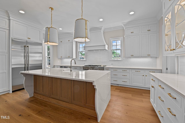 kitchen with decorative light fixtures, light hardwood / wood-style flooring, backsplash, custom range hood, and built in fridge