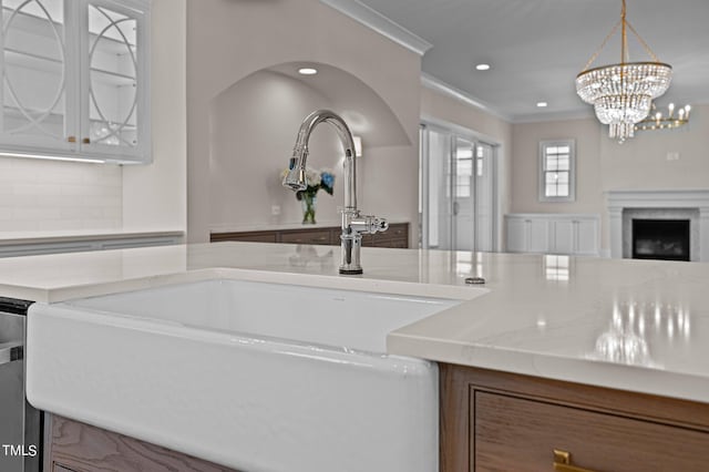 kitchen featuring pendant lighting, light stone countertops, ornamental molding, sink, and tasteful backsplash