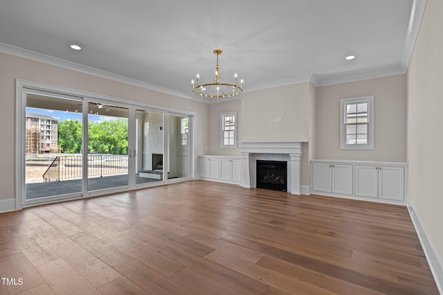 unfurnished living room featuring a fireplace, a notable chandelier, crown molding, and hardwood / wood-style flooring