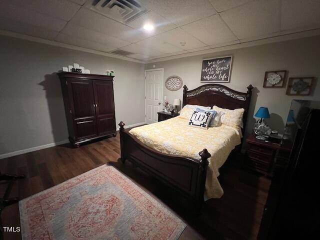 bedroom with dark hardwood / wood-style floors, a drop ceiling, and ornamental molding